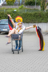 Weiblicher und männlicher Fußballfan feiern auf Supermarktparkplatz den Sieg der deutschen...