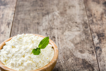Fresh cottage cheese in a wooden bowl on wooden table. Copyspace
