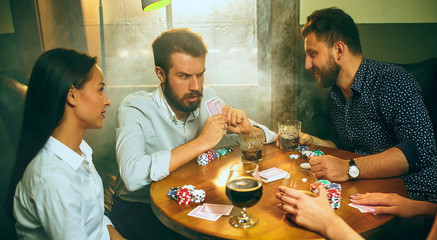 Side view photo of friends sitting at wooden table. Friends having fun while playing board game.