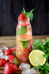 Lemonade with strawberry, lime, ice cubes and mint in a glass bottle
