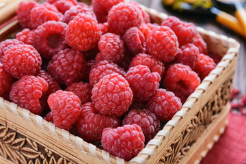 Raspberry in a basket is on a wooden table next to wooden spoons