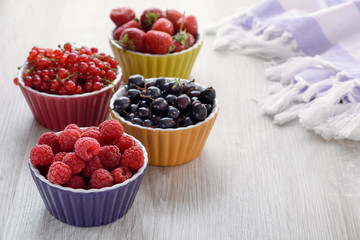 Raspberries, strawberries, currants red and black in colored bowls are on the table