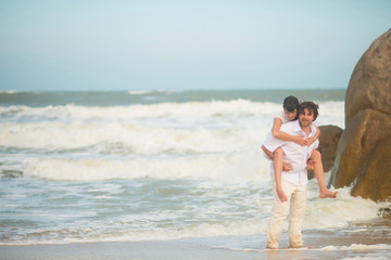 The groom carries the bride on his back against the sea and rocks
