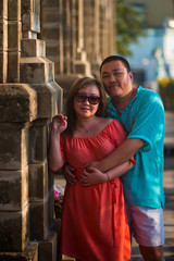 Portrait of an adult Asian couple who hugs near a column at sunset