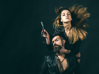 Barber concept. Couple of sexy girl and brutal bearded hipster with mustache, black background. Barber with straight razor works on haircut. Hipster with beard and sexy girl holds straight razor