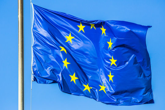 Flag of Europe blue color with yellow stars waving in the wind on blue sky.
