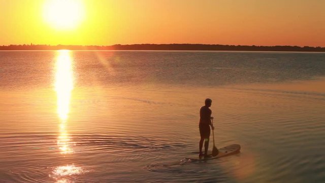 Man paddling in open water at sunset. Looping movie