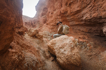 Beautiful young girl in hare, hat and with backpack travels among sands in wild
