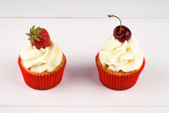 Two red cupcakes with white cream decorated with strawberry and cherry on white background. Picture for a menu or a confectionery catalog.