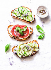 Summer variations of sandwiches - with cream cheese, avocado, tomato and cucumber on a light background, top view. Healthy diet food concept. Flat lay, copy space