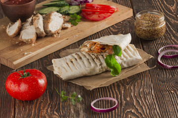 Shaurma, cut in half, meat with vegetables in a bread cake, top view on an old wooden rustic background, on a wooden board with tomato and pepper, copy space
