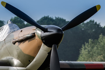 A photograph documenting the propeller and shroud covering the cockpit of an RAF Hawker Hurricane as stands on an airstrip under blue skies waiting to be flown. - obrazy, fototapety, plakaty