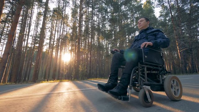 Physically challenged man is moving in a powered wheelchair along the road