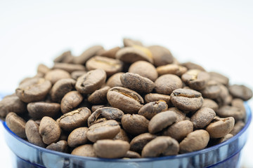 Close up of coffee bean in clear blue plastic cup with white background.