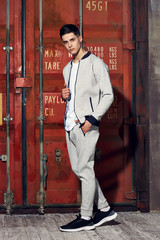 Young handsome sporty man in gary sport clothes posing against red metal doors of intermodal container