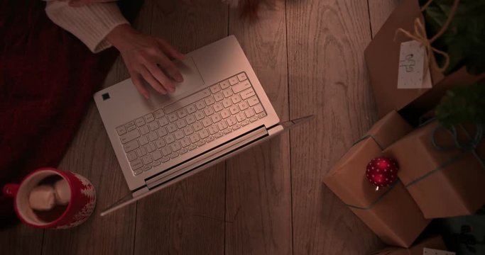 Young redhead woman shopping online using using laptop under Christmas tree