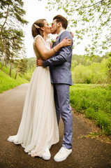 Naklejka premium Bride and groom hugging and kissing, standing on the path in the background of nature