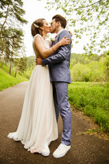 Bride and groom hugging and kissing, standing on the path in the background of nature
