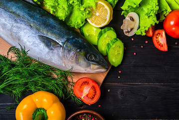 Raw fish and ingredients: lemon, spices, greens, tomato, on a wooden table, top view.