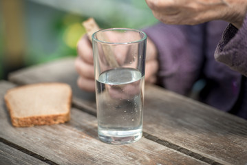 The old woman drinks water and eats bread at an old wooden table in a garden