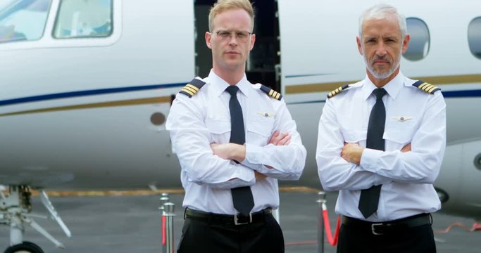 Two male pilots standing with arms crossed on a runway 4k