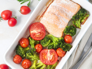 Fish salmon baked in oven with vegetables, broccoli. Healthy diet food, white marble backdrop, top view, close-up