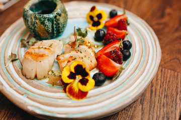 delicious sea bass with strawberry, blueberry and raspberry sauce decorated with flowers on a beautiful clay plate at the wedding dinner.