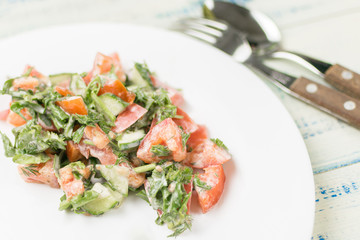 Salad of fresh vegetables - cucumber, tomato, greens with sour cream.