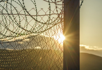 Shine of the sun through the fence with barbed wire