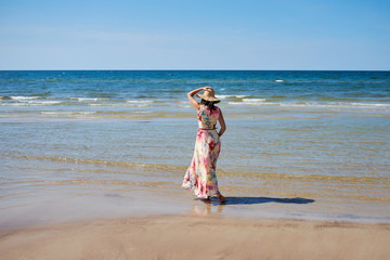 A relaxed girl with a hat goes along the beach.
