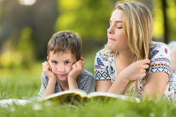 Mother and son in park outdoosr on a blanket reading a book