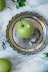 Green apple with leaf and flowers on white marble background.