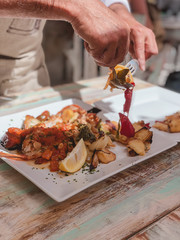 manos de hombre, cocinero de restaurante, preparando y repartiendo pescado tipico de ibiza, en los platos de los comensales