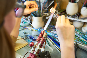 Close up of  female hands shaping glass over gas torch while making handmade beads in modern creative workshop, copy space