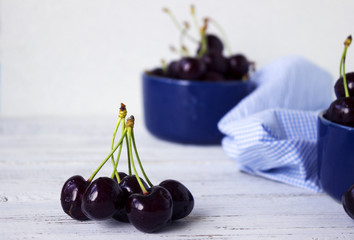 Ripe cherries in a blue bowl, dark-berries in deep plates. Fruits, vegetarian food
