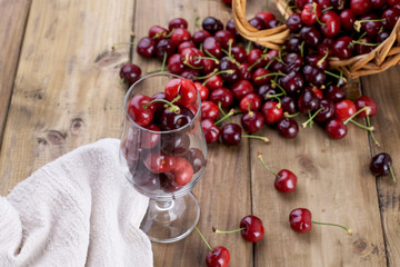 A large basket of ripe cherries and scattered berries on a table and in a glass. Wooden background, free space for text. Retro style. Copy space