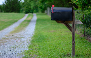 Rural mailbox with flag raised along a gravel road.