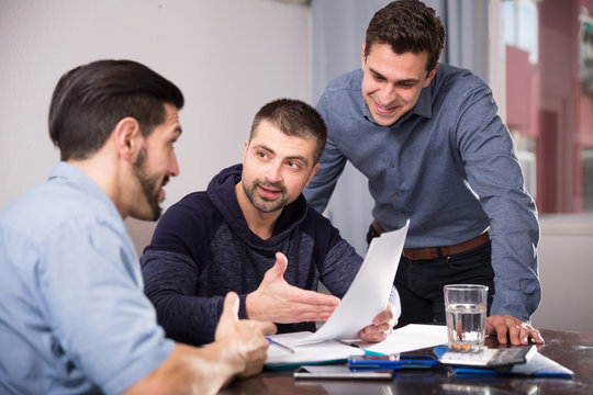 Two positive men helping friend with documents at table