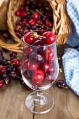 A large basket of ripe cherries and scattered berries on a table and in a glass. Wooden background, free space for text. Retro style. Copy space
