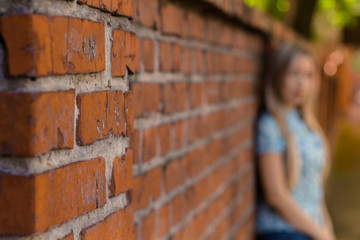Blured girl standing near the brick wall and waiting. Blured background