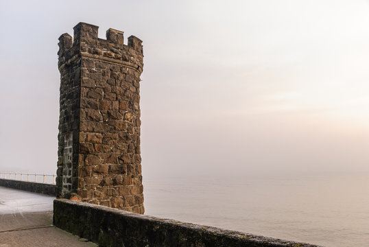 Stone castlated tower on a sea wall on a misty morning
