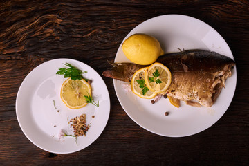 Baked fish with lemon, spices and herbs on white plate on wooden background without head