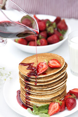 Woman hand pour a syrup on pancakes .Homemade pancakes with fresh strawberries