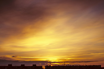 Beautiful cloudy dramatic morning sky above silhouette of city buildings. Picturesque dawn in city. Aircraft trail on vivid clouds. Background from unimaginable fantasy sunrise in heaven.