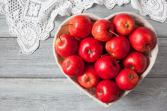 Red apples in a basket shaped like heart on a table