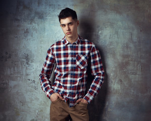 Portrait of young trendy handsome man with short dark hair wearing checkered shirt and brown...