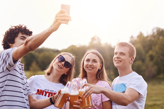 Two teenage girls and boys pose for selfie while have picnic outdoor, going to share photos in social networks, have happy expressions, enjoy summer time together. People, fun, youth, friendship
