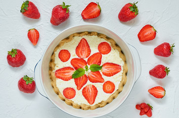 Homemade raw strawberry cheesecake in a baking dish on the white background. Vegetarian healthy raw tart decorated with mint leaves and strawberries. Delicious summer dessert. Top view