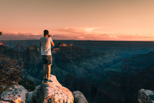 young man stays on the edge of the rock and takes a picture of Magnificent Grand Canyon, Arizona, USA.