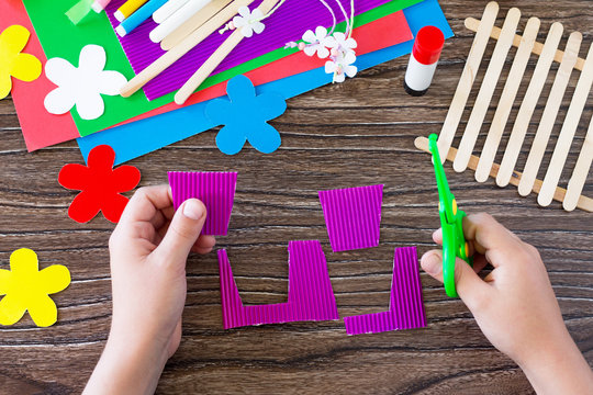 A child is cutting details of a gift of summer flowers on a wooden sticks fence. Handmade. Project of children's creativity, handicrafts, crafts for kids.